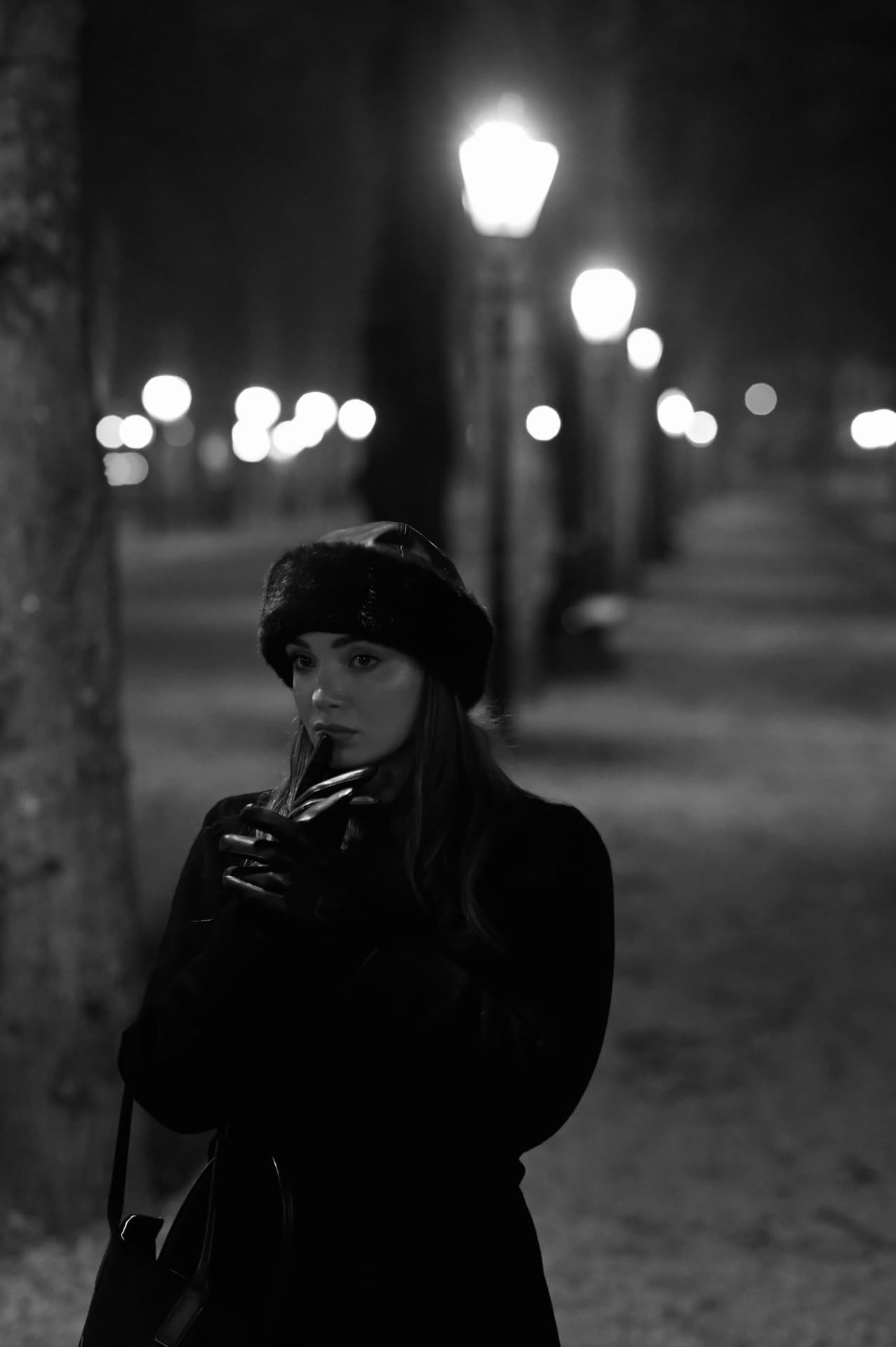 Black and white portrait of a woman in a winter coat on a lamp-lit street