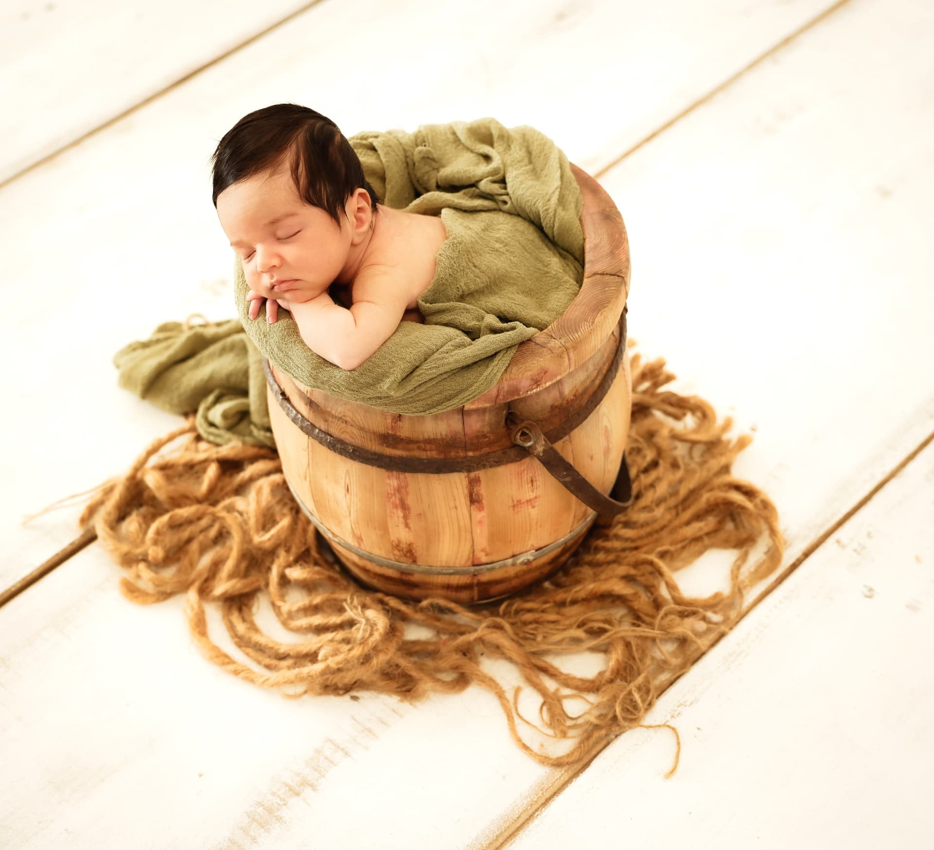 Newborn baby sleeping in a wooden bucket with a green wrap