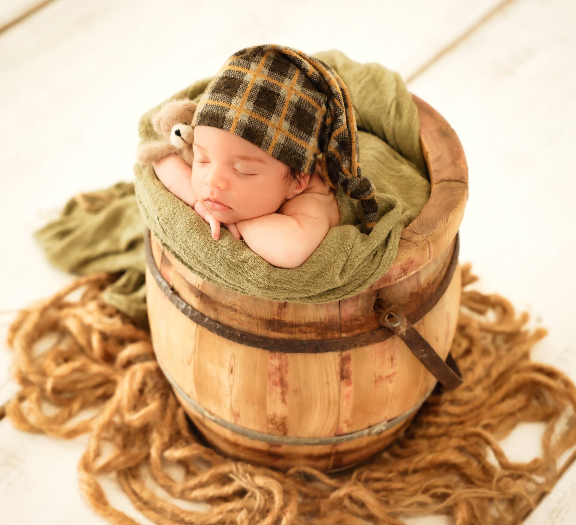 Newborn baby in a knitted cap resting in a wooden bucket