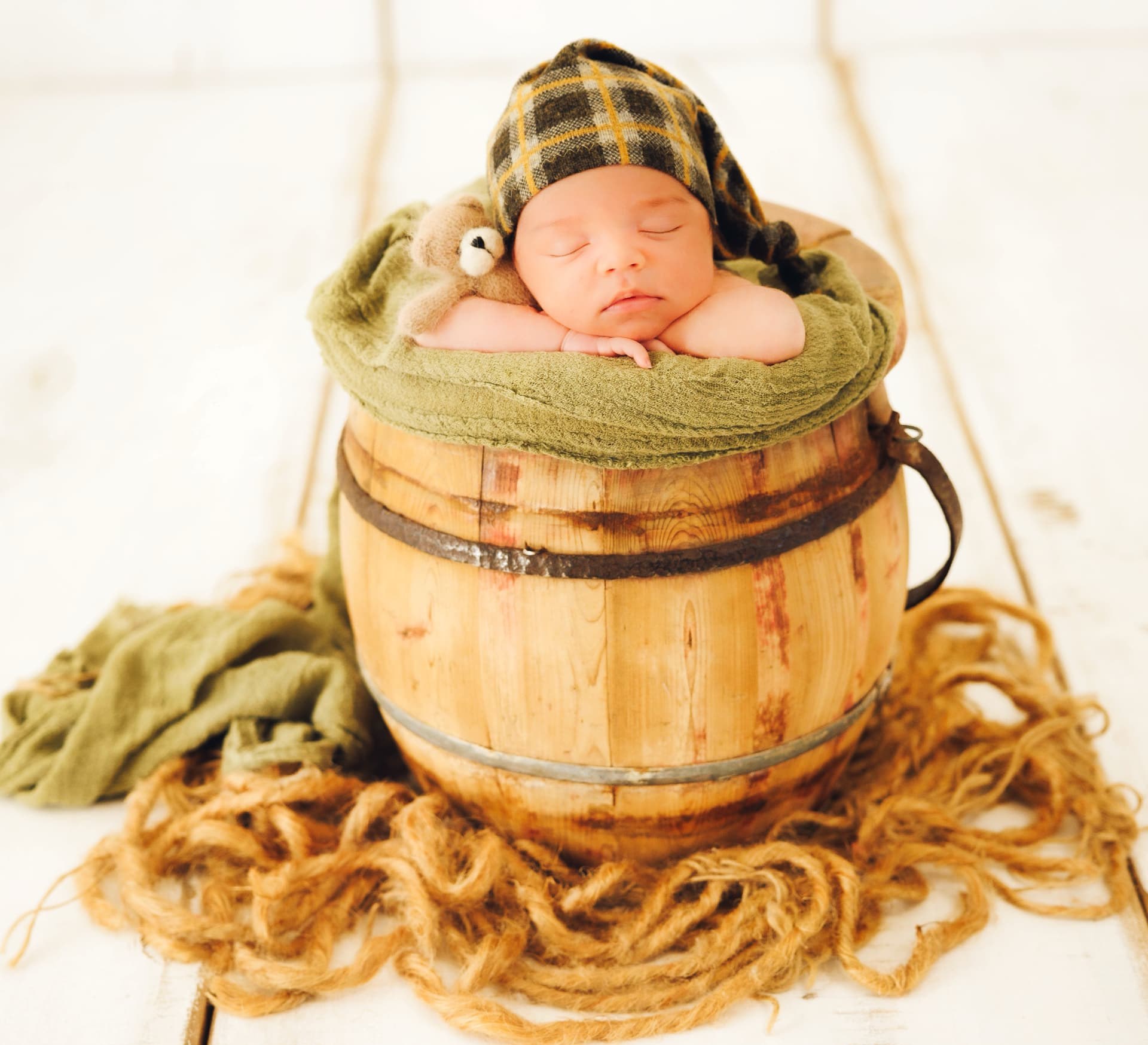 Newborn baby with a teddy bear in a wooden bucket