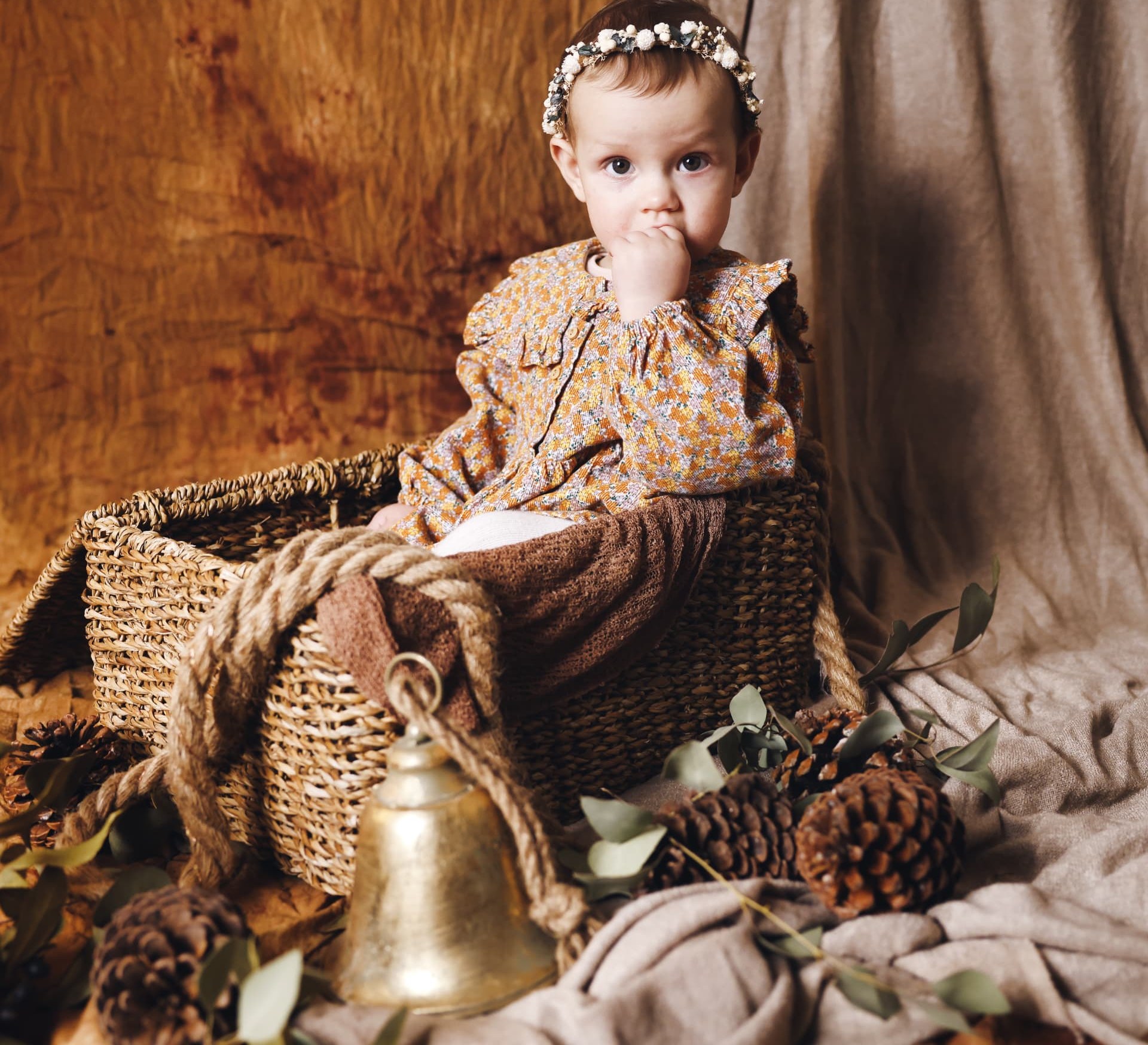 Toddler girl in a basket with pine cones and eucalyptus