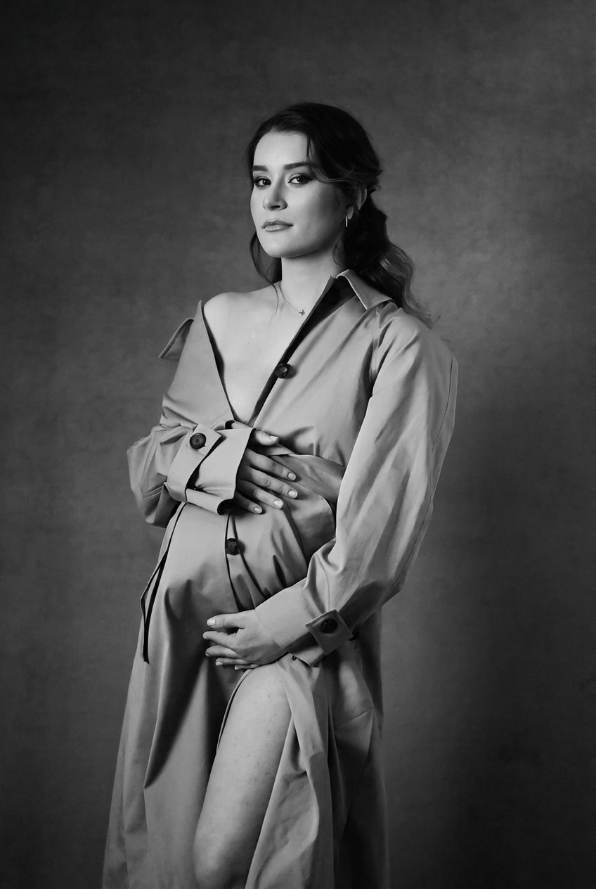 Expectant mother in a trench coat against a warm ochre backdrop