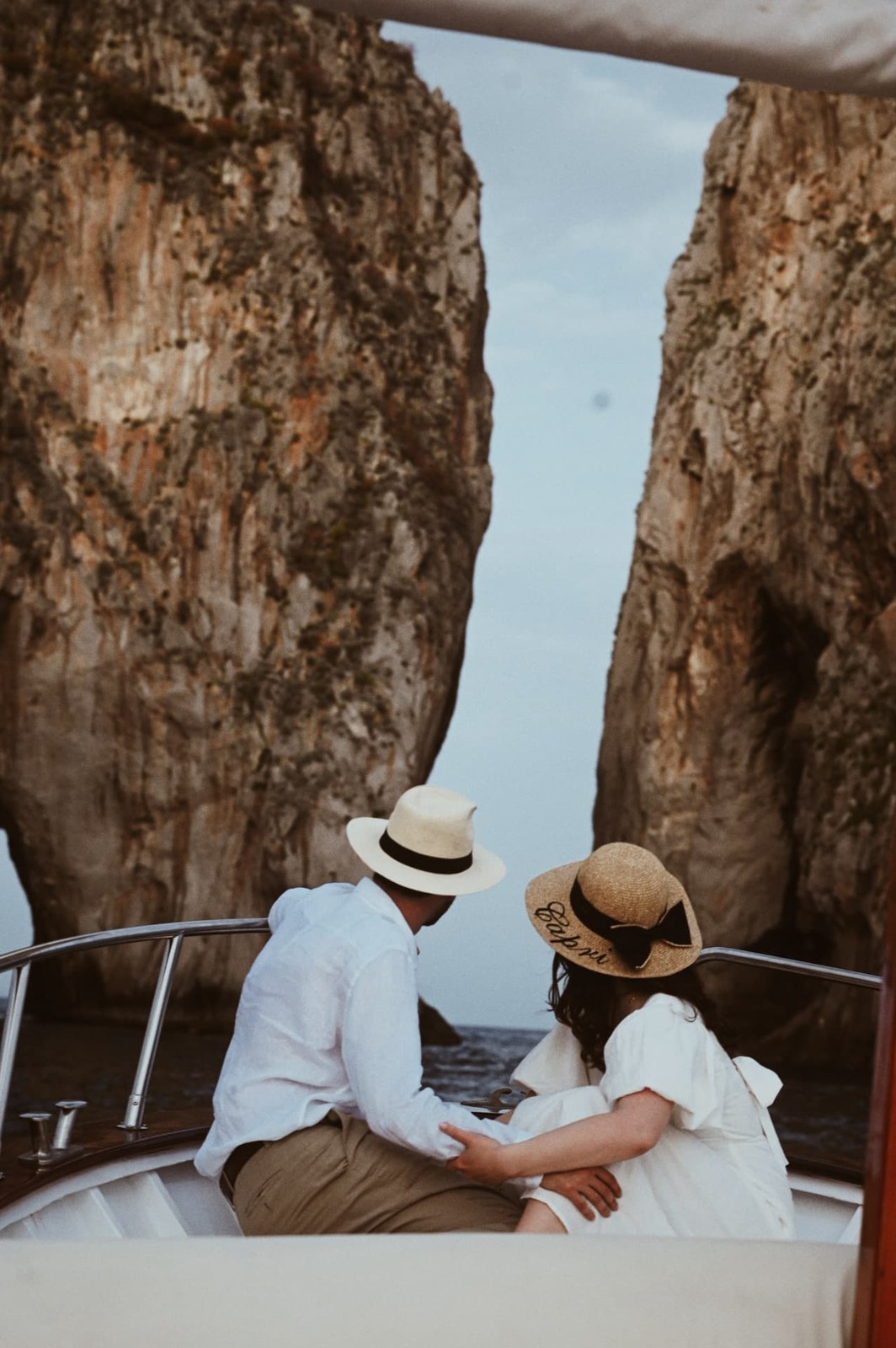 Couple in straw hats on a boat looking out at sea cliffs