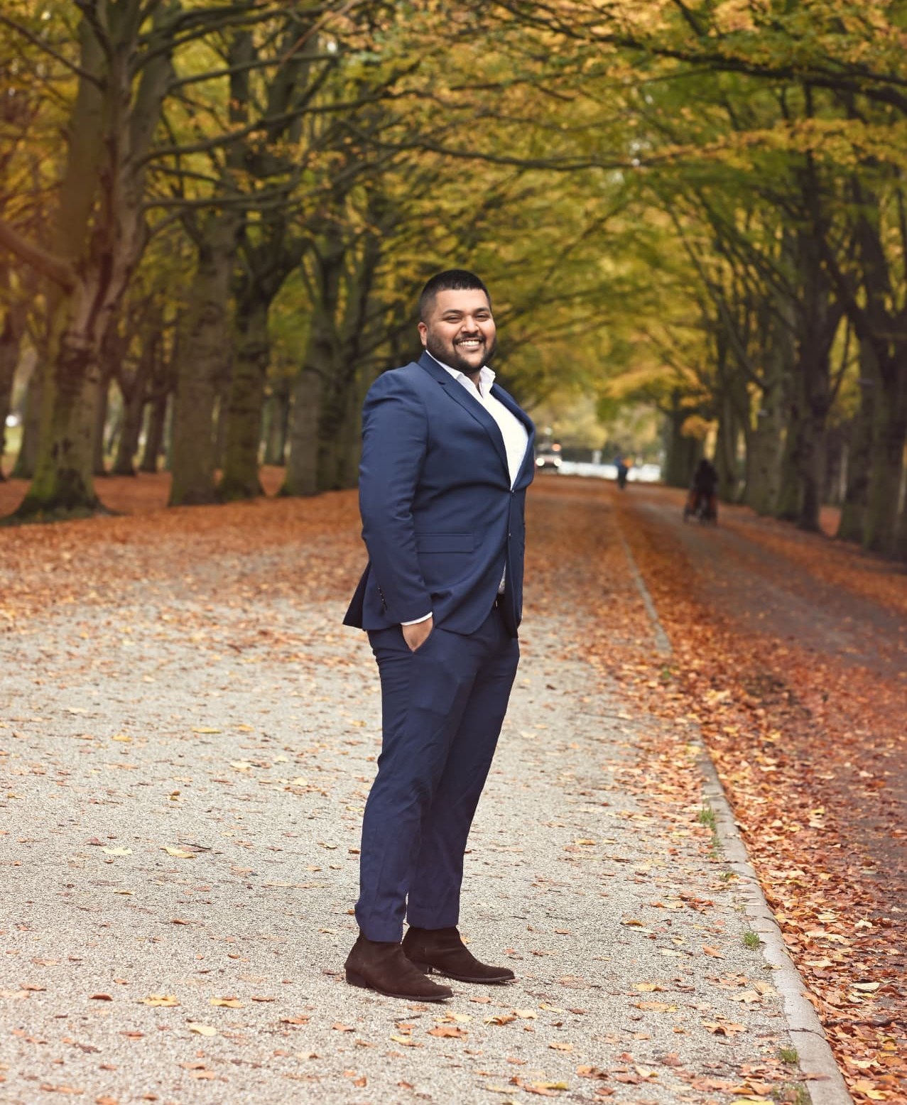 Man in a navy suit on a tree lined autumn path