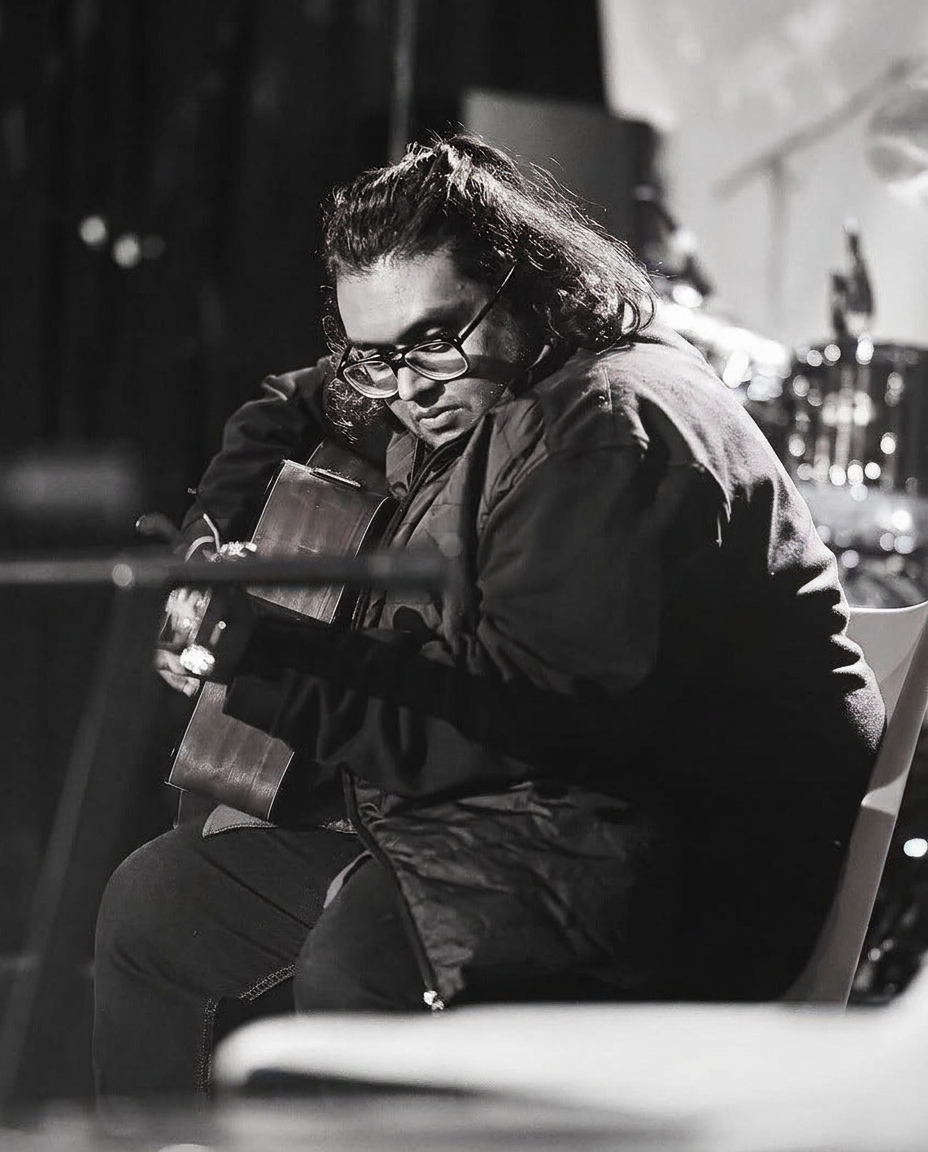 Musician playing acoustic guitar under warm stage light