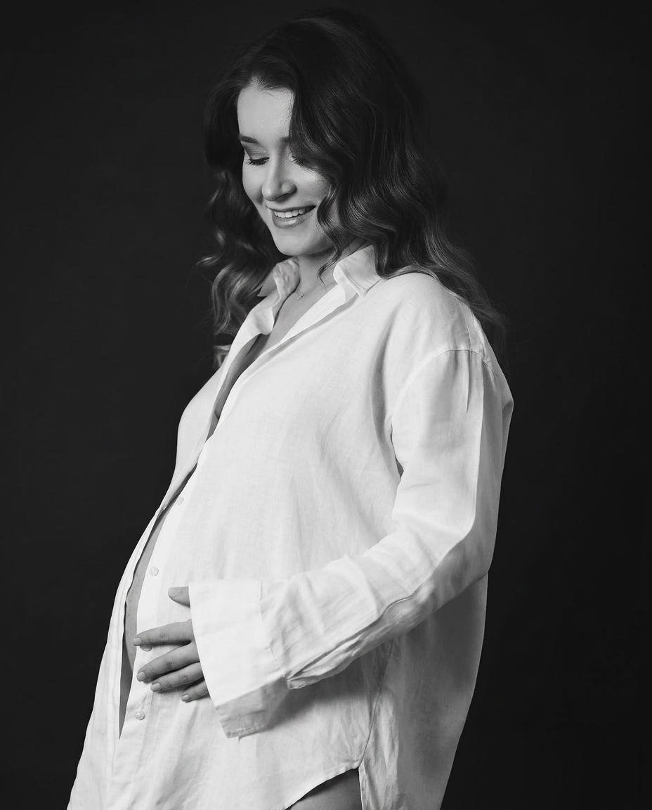 Expectant mother in a white shirt against a dark backdrop