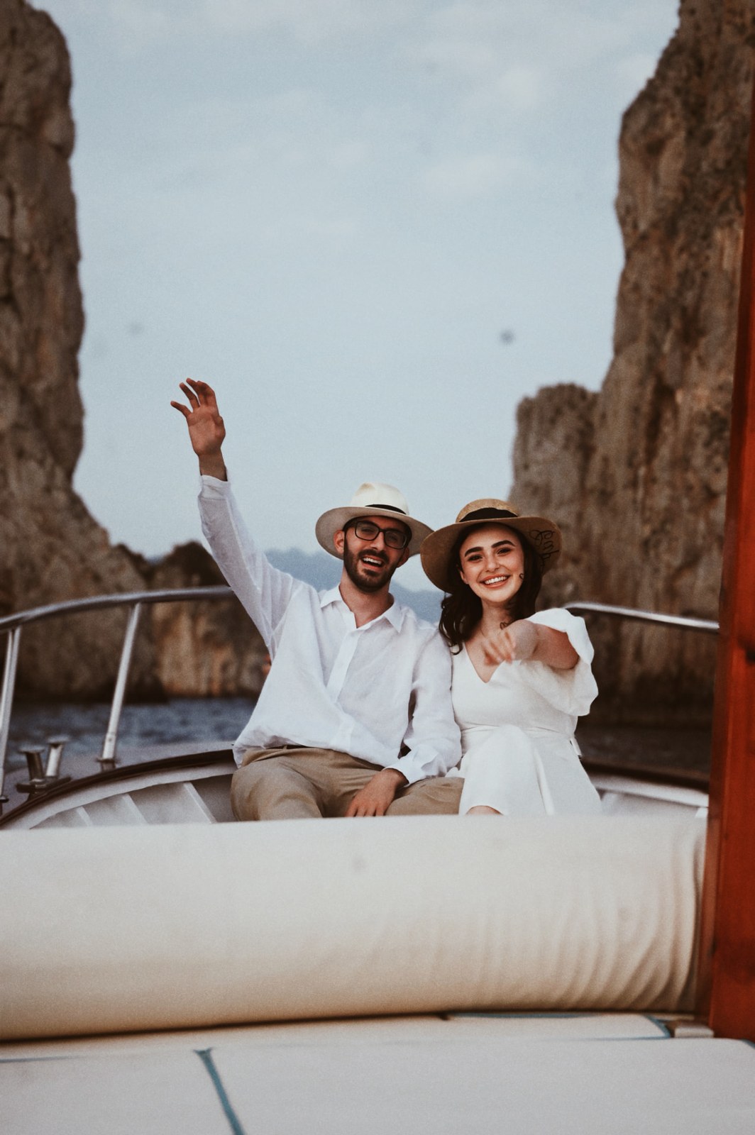 Couple laughing and waving from a boat between the Faraglioni