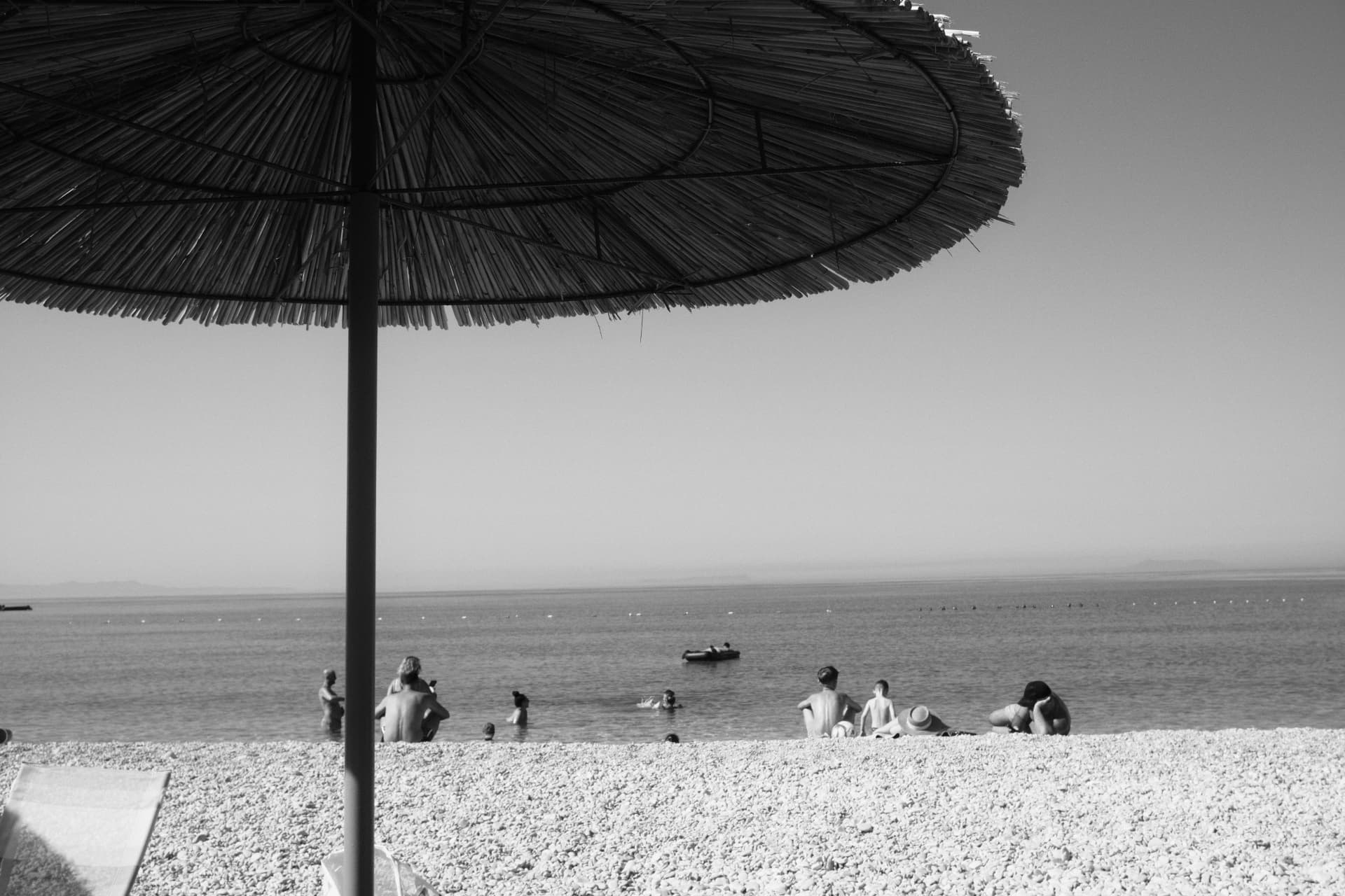 Black and white view of the sea from under a straw beach umbrella
