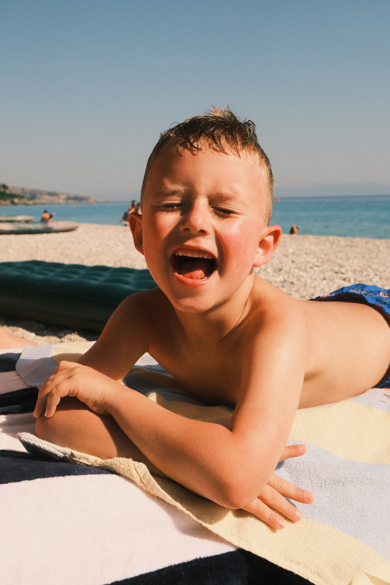 Boy laughing on a striped towel at a pebble beach